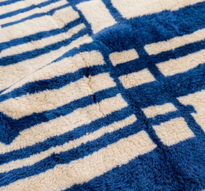 Full view of custom Beni Mrirt rug hanging, featuring bold Majorelle blue and cream abstract geometric design. Hand-knotted Middle Atlas wool carpet by Craftily Marrakech.
